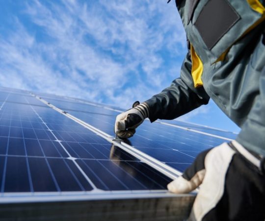 Close up of man technician in work gloves installing stand-alone photovoltaic solar panel system under beautiful blue sky with clouds. Concept of alternative energy and power sustainable resources.